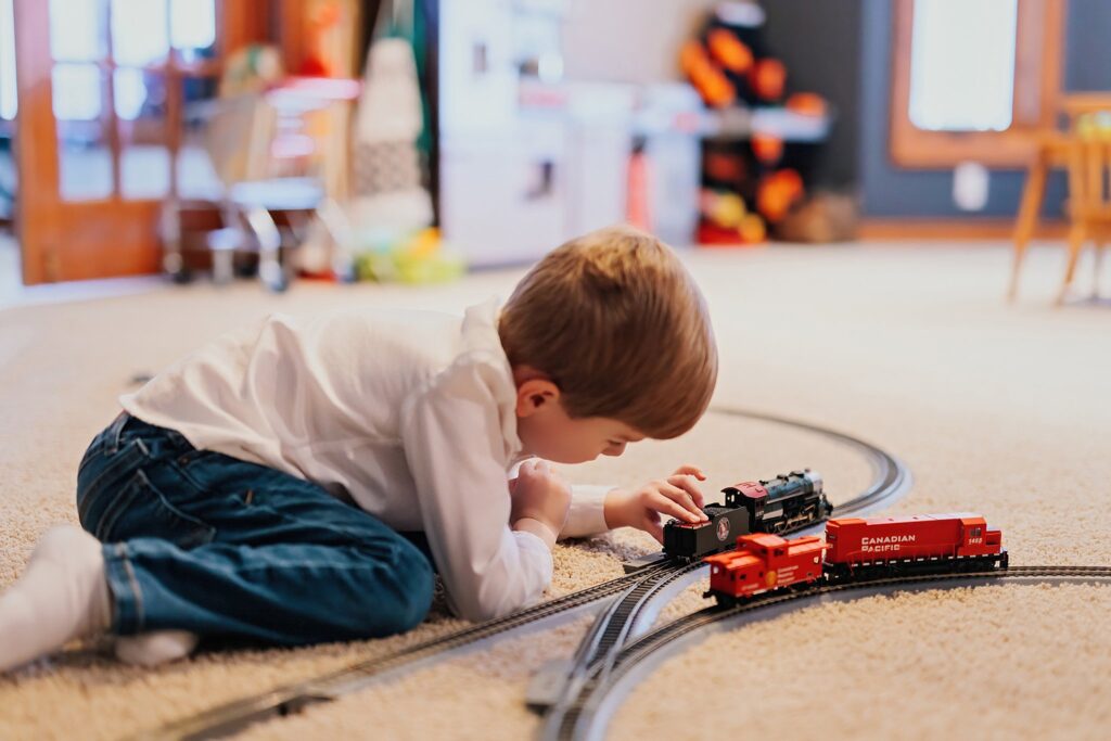 A close up of a small boy in his home playing with a train set on the carpet