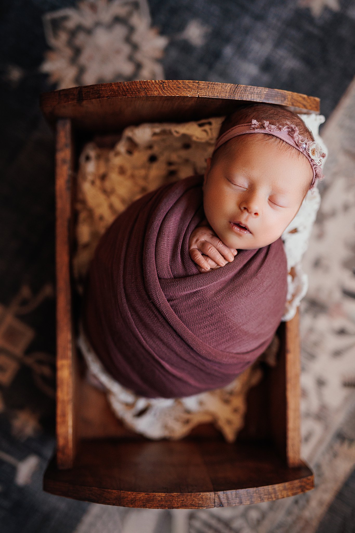 a peaceful newborn wrapped in mauve and cradled in lace in a wooden bed