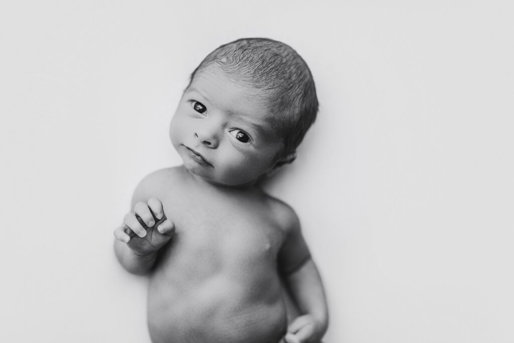 a black and white photo of an awake and alert newborn baby boy looking at the camera