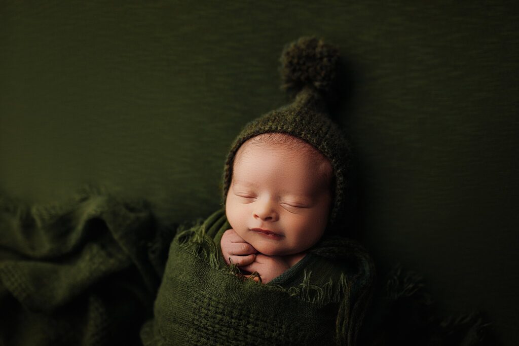a baby in deep olive green bonnets and wraps at a newborn session in cedar falls iowa newborn photography at nicole harnois photography studio