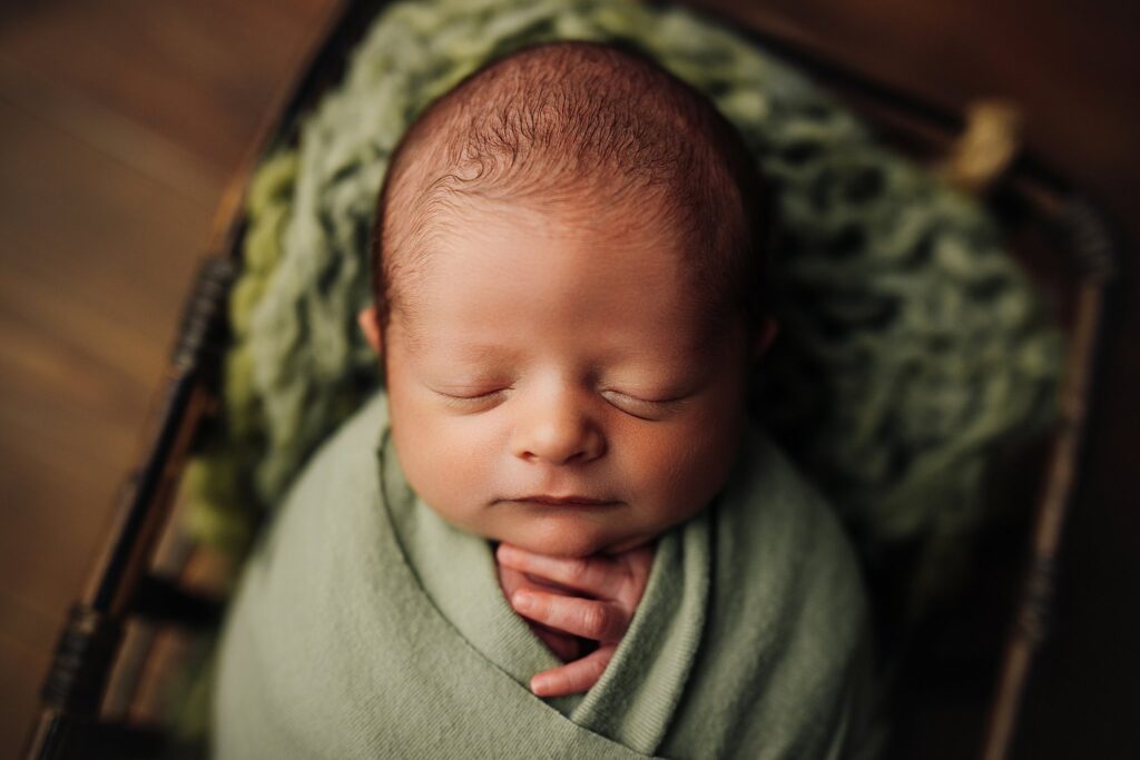 a newborn baby boy sleeps in a soft green set up at a studio newborn session