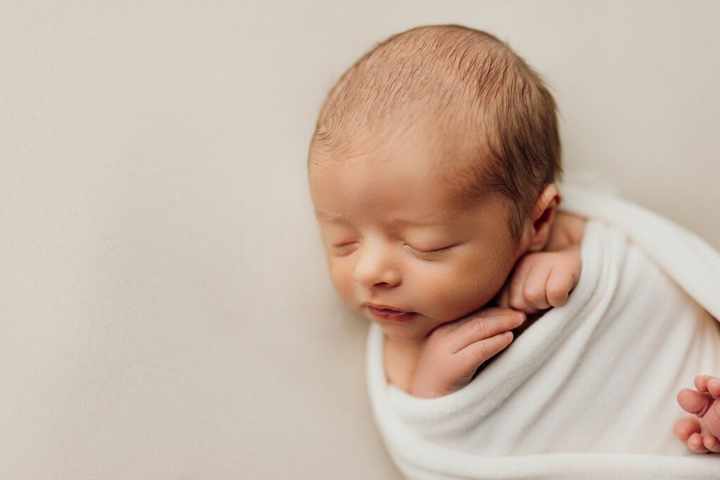 a newborn baby boy sleeps while wrapped in a cream wrap