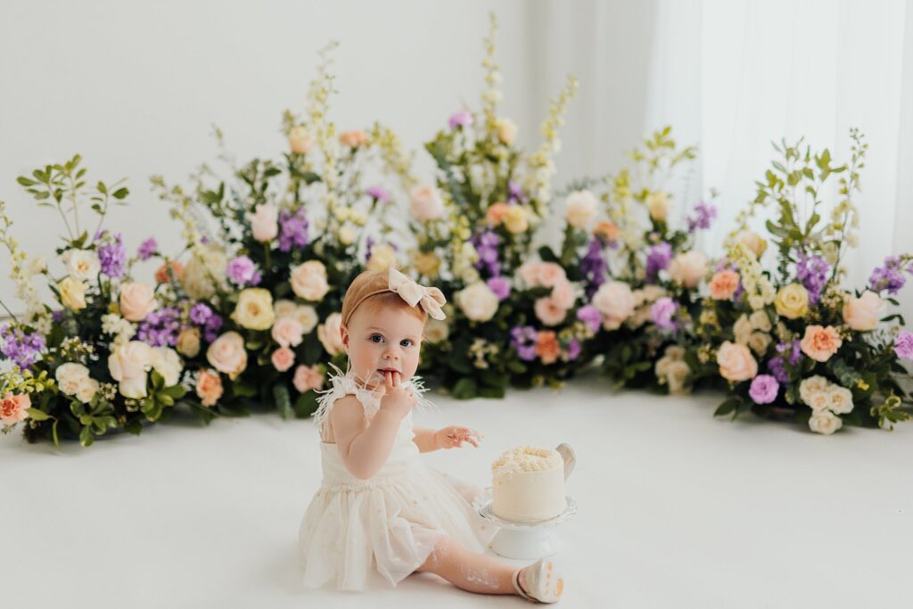 One-year-old baby enjoying a cake smash session with fresh florals in a Cedar Falls, Iowa photography studio