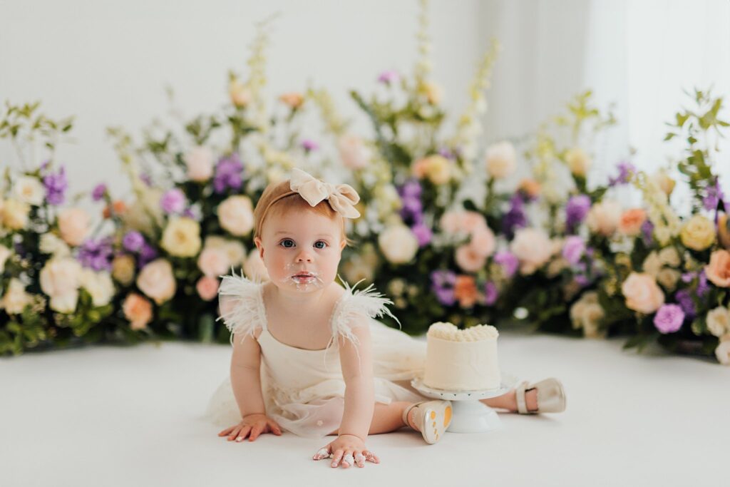 One-year-old baby enjoying a cake smash session with fresh florals in a Cedar Falls, Iowa photography studio