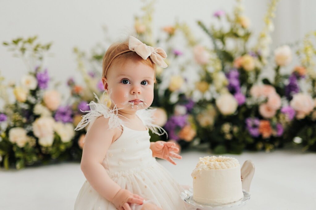 One-year-old baby enjoying a cake smash session with fresh florals in a Cedar Falls, Iowa photography studio