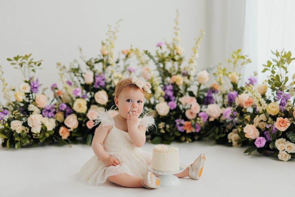 One-year-old baby enjoying a cake smash session with fresh florals in a Cedar Falls, Iowa photography studio