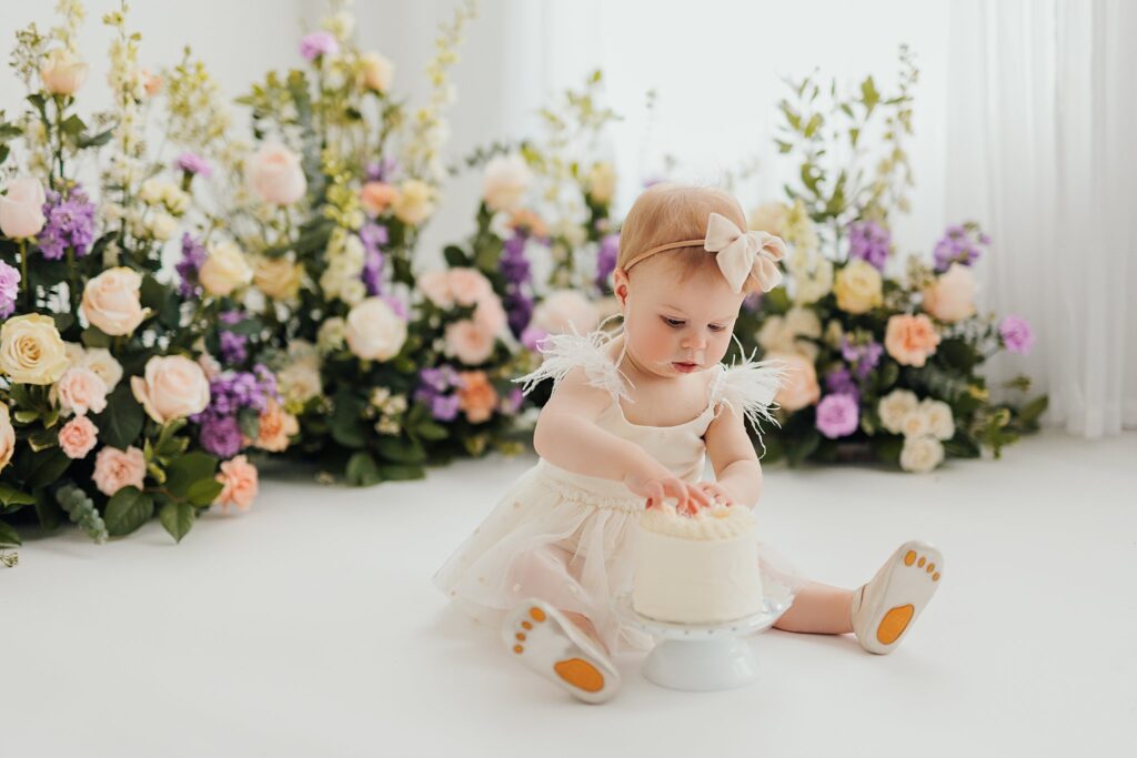 One-year-old baby enjoying a cake smash session with fresh florals in a Cedar Falls, Iowa photography studio