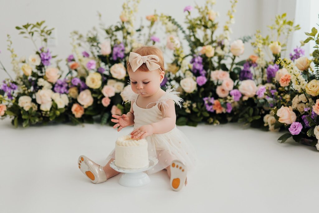 One-year-old baby enjoying a cake smash session with fresh florals in a Cedar Falls, Iowa photography studio