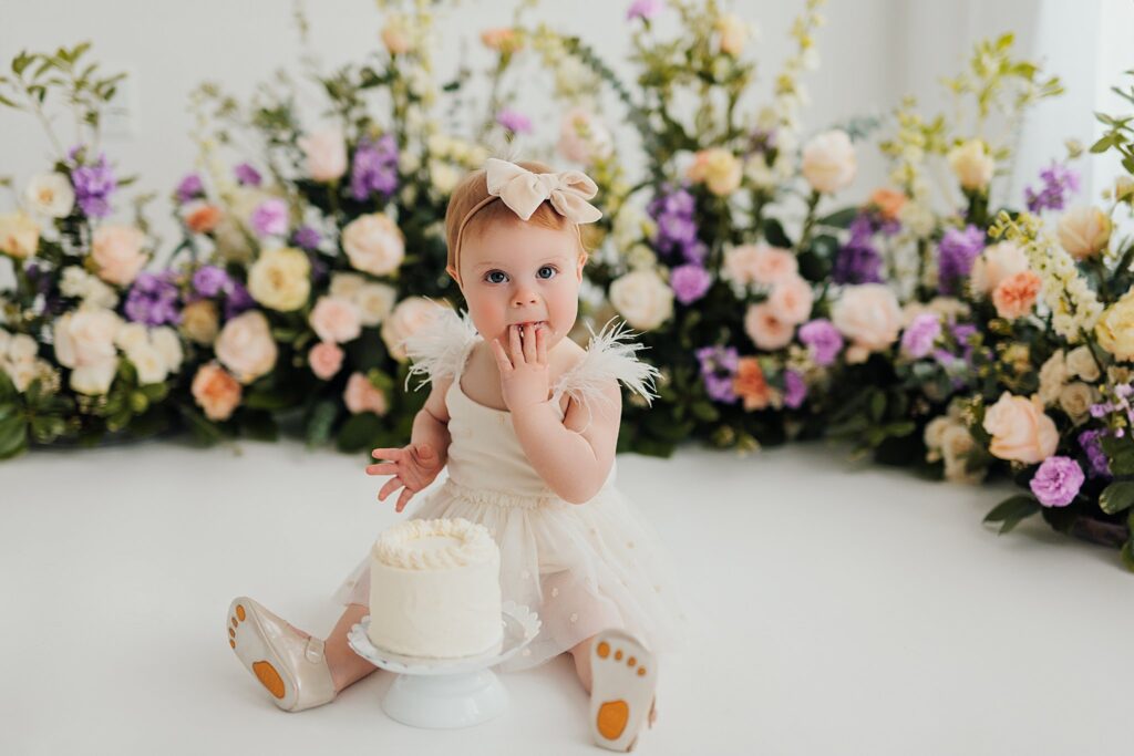 One-year-old baby enjoying a cake smash session with fresh florals in a Cedar Falls, Iowa photography studio