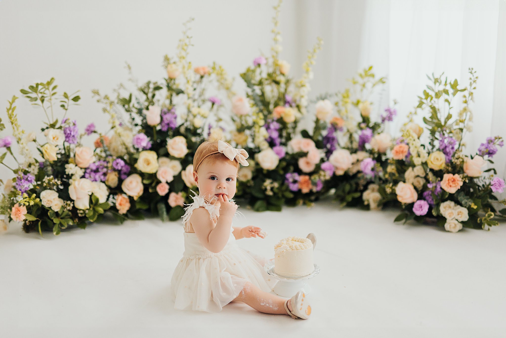 One-year-old baby enjoying a cake smash session with fresh florals in a Cedar Falls, Iowa photography studio