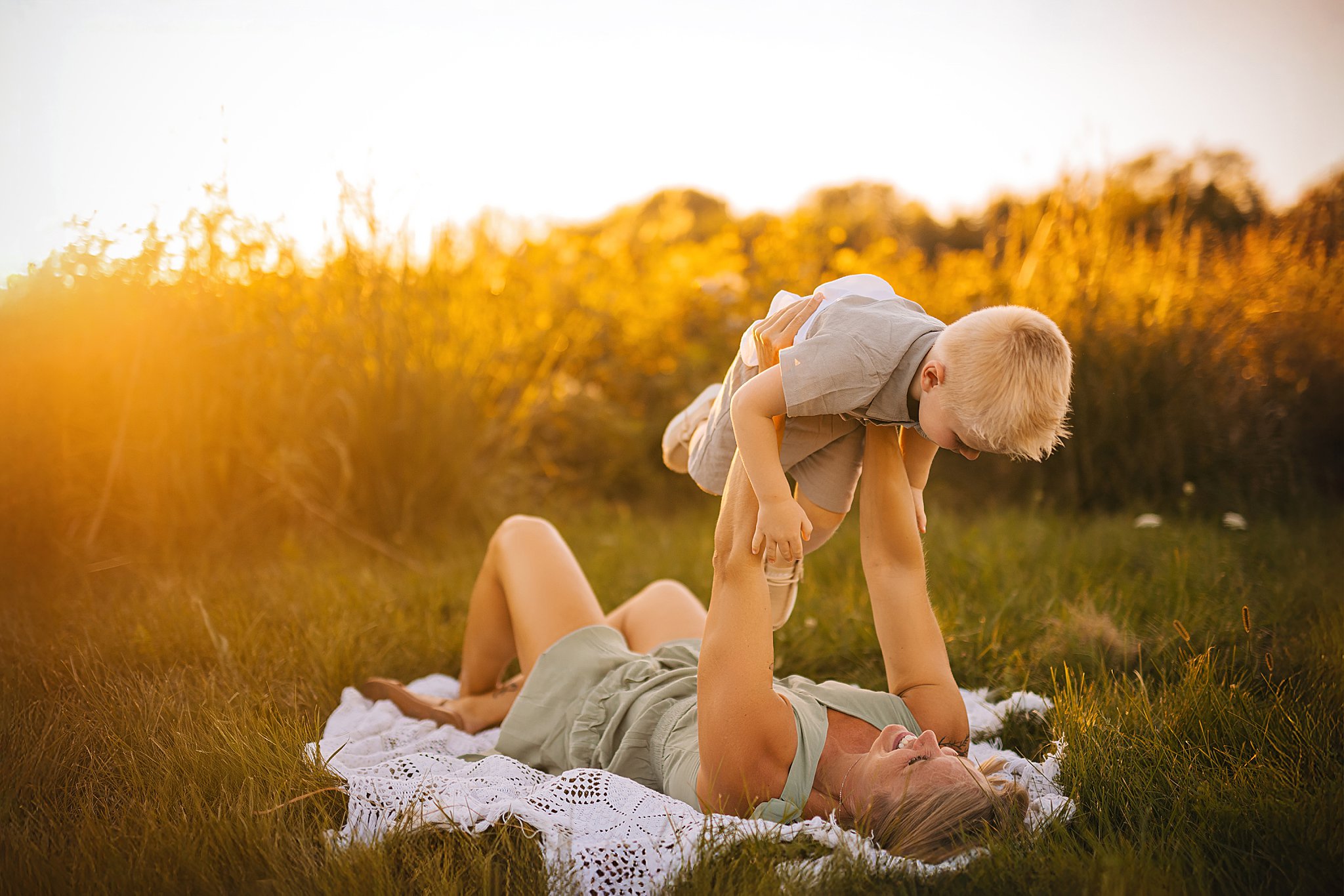 a small boy is held over his mother in a sunset field
