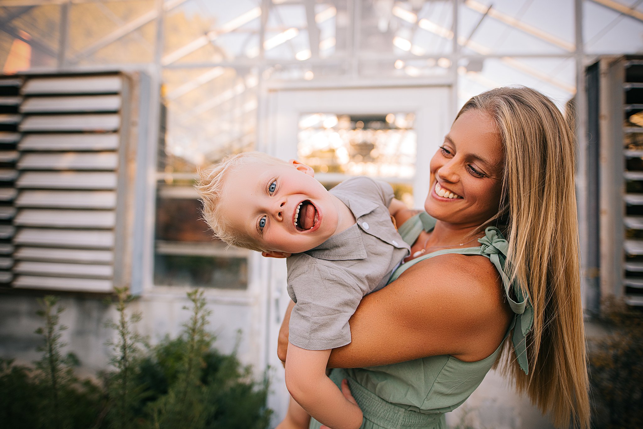 a mother and son cuddlign in front of a greenhouse